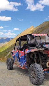 Red off-road buggy on a mountain dirt road with green hills and blue sky