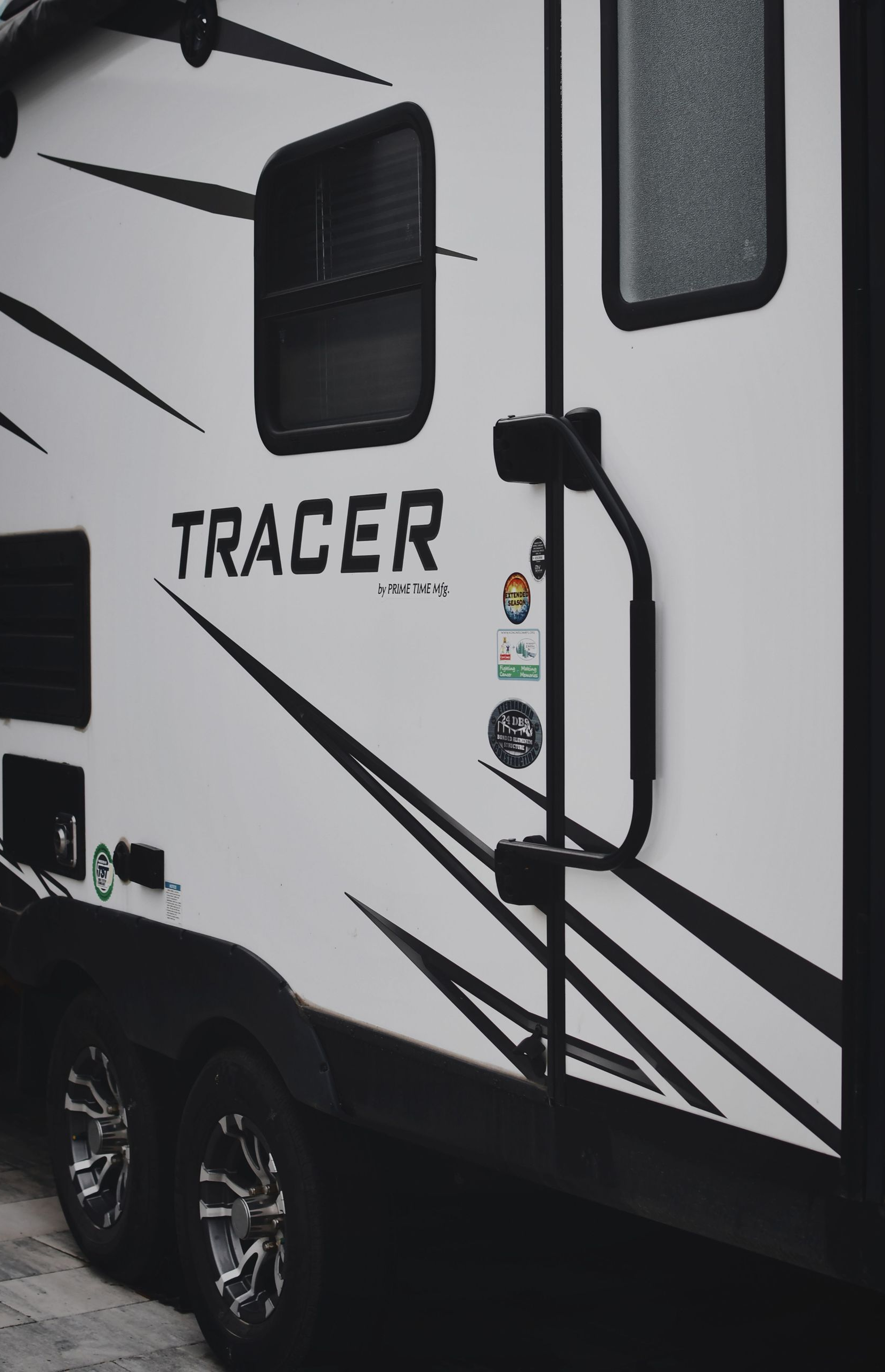 White Tracer RV side with black graphics and door, parked on pavement.