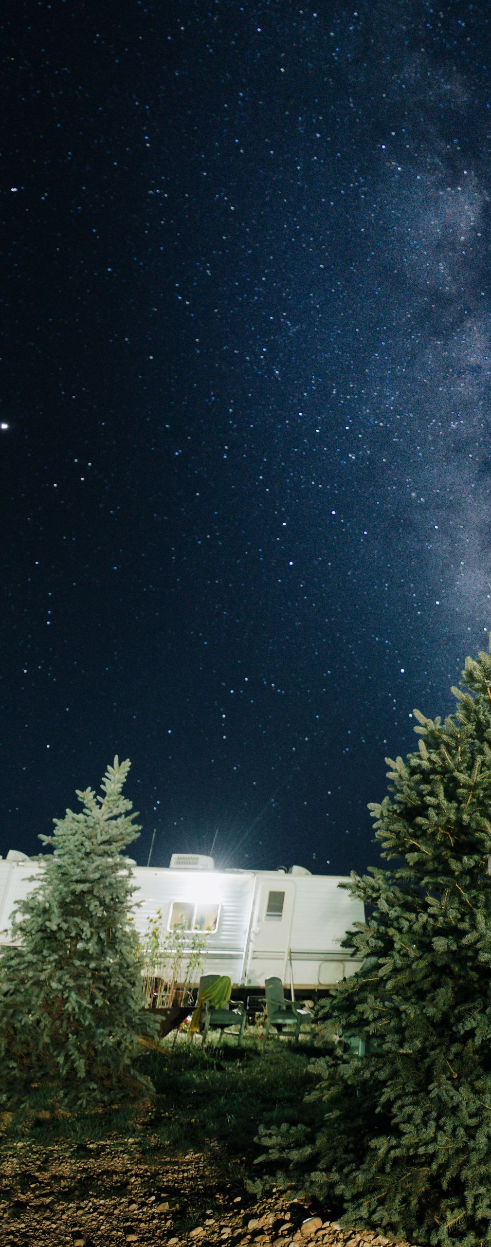 Starry night sky above a lit house and trees, with the Milky Way visible overhead