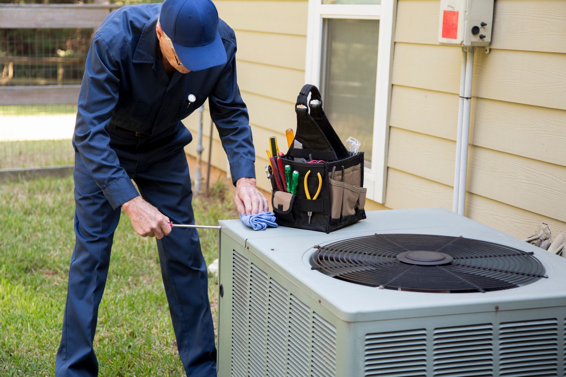 A man is working on an air conditioner outside of a house. A man is working on an air conditioner outside of a house.