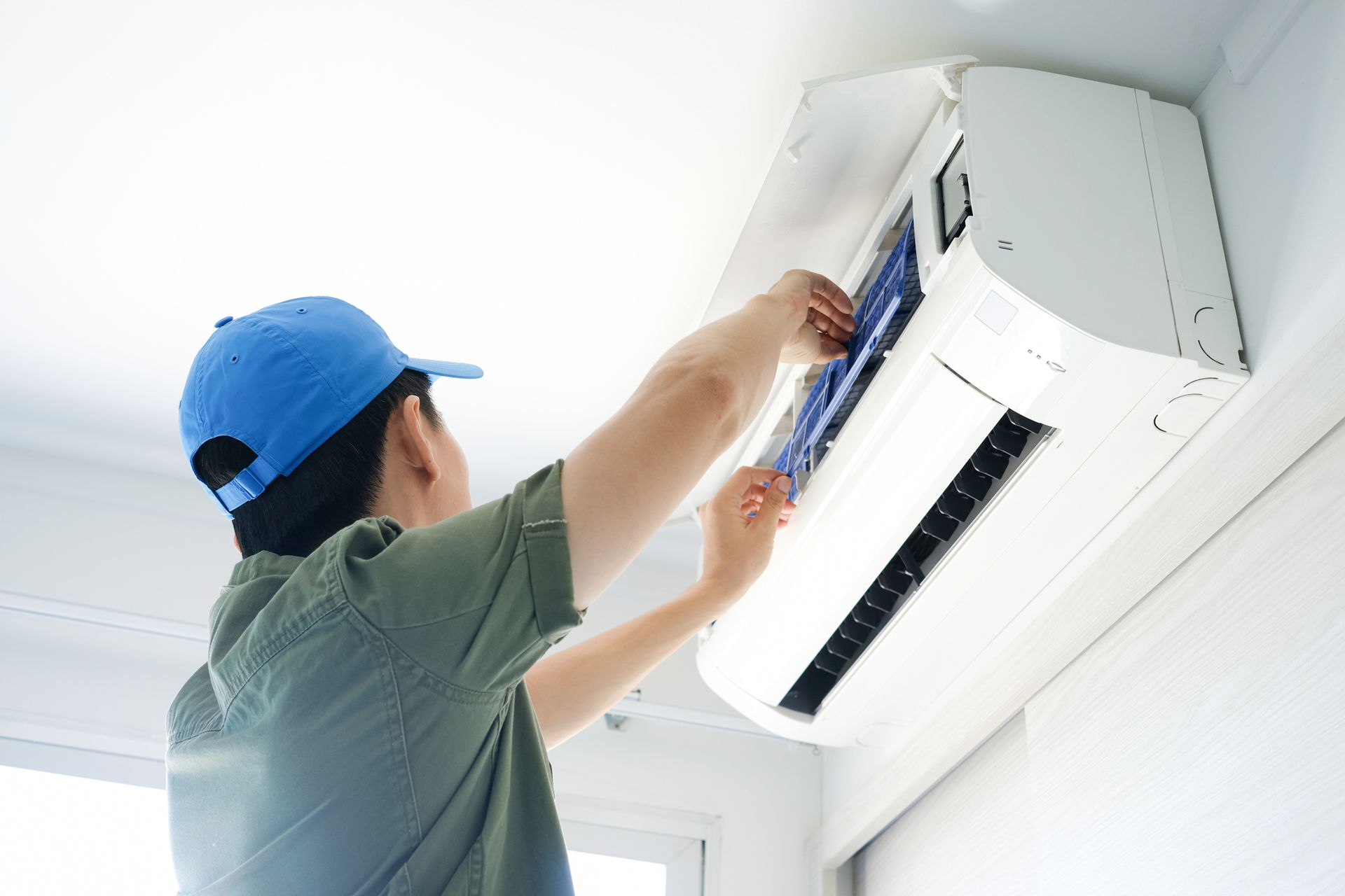A man in a blue hat is cleaning an air conditioner.