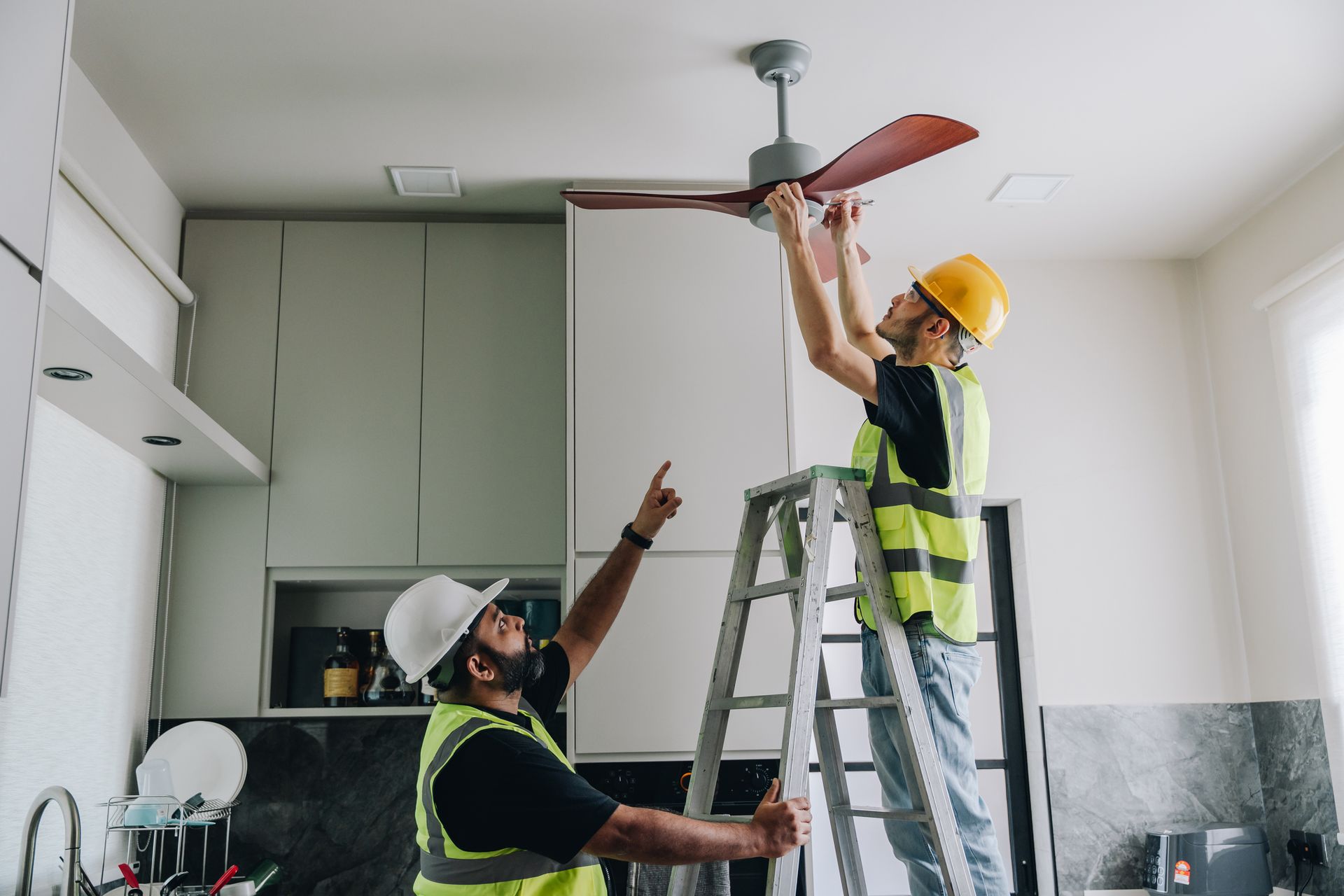 Two men are working on a ceiling fan in a kitchen. Two men are working on a ceiling fan in a kitchen.