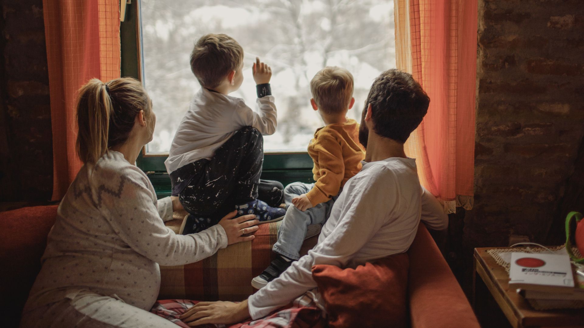 A family is sitting on a couch looking out a window. A family is sitting on a couch looking out a window.