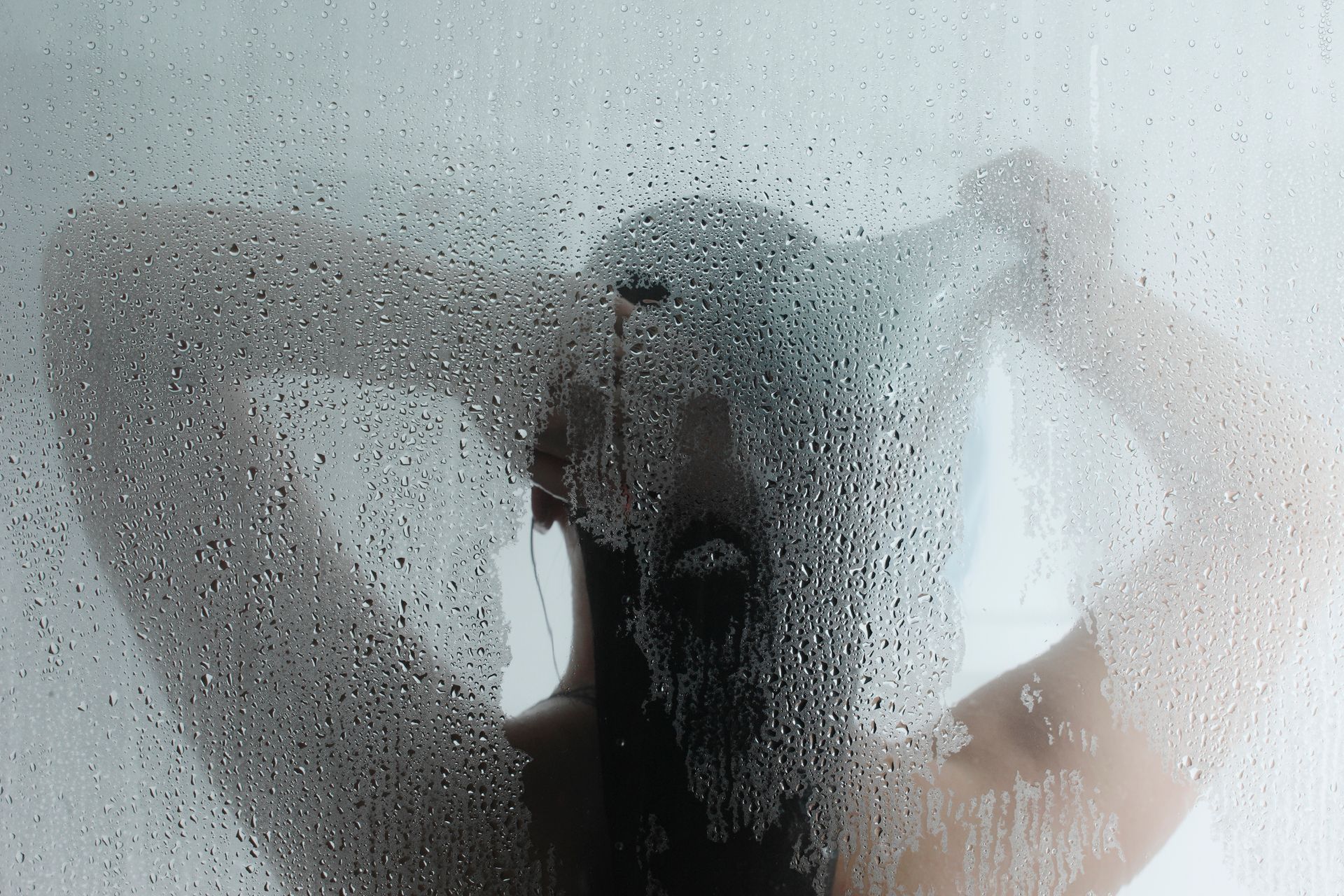 A woman is taking a shower behind a window with water drops on it.