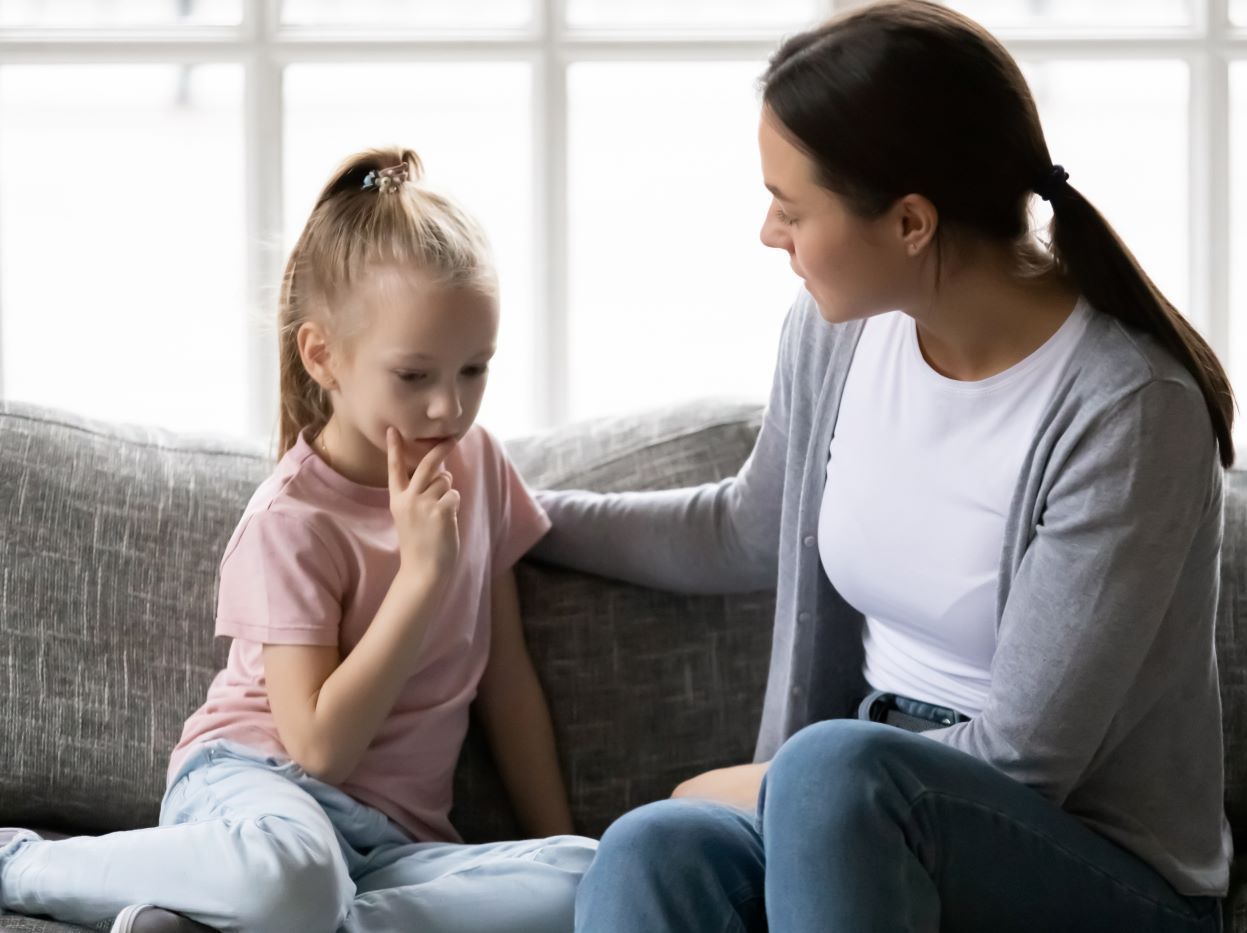 A woman is sitting on a couch talking to a little girl.