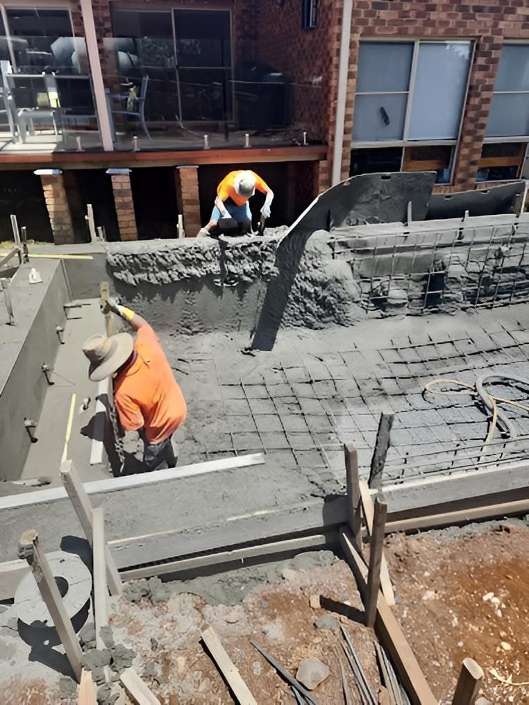 Workers pouring and levelling concrete for a swimming pool at a family home.