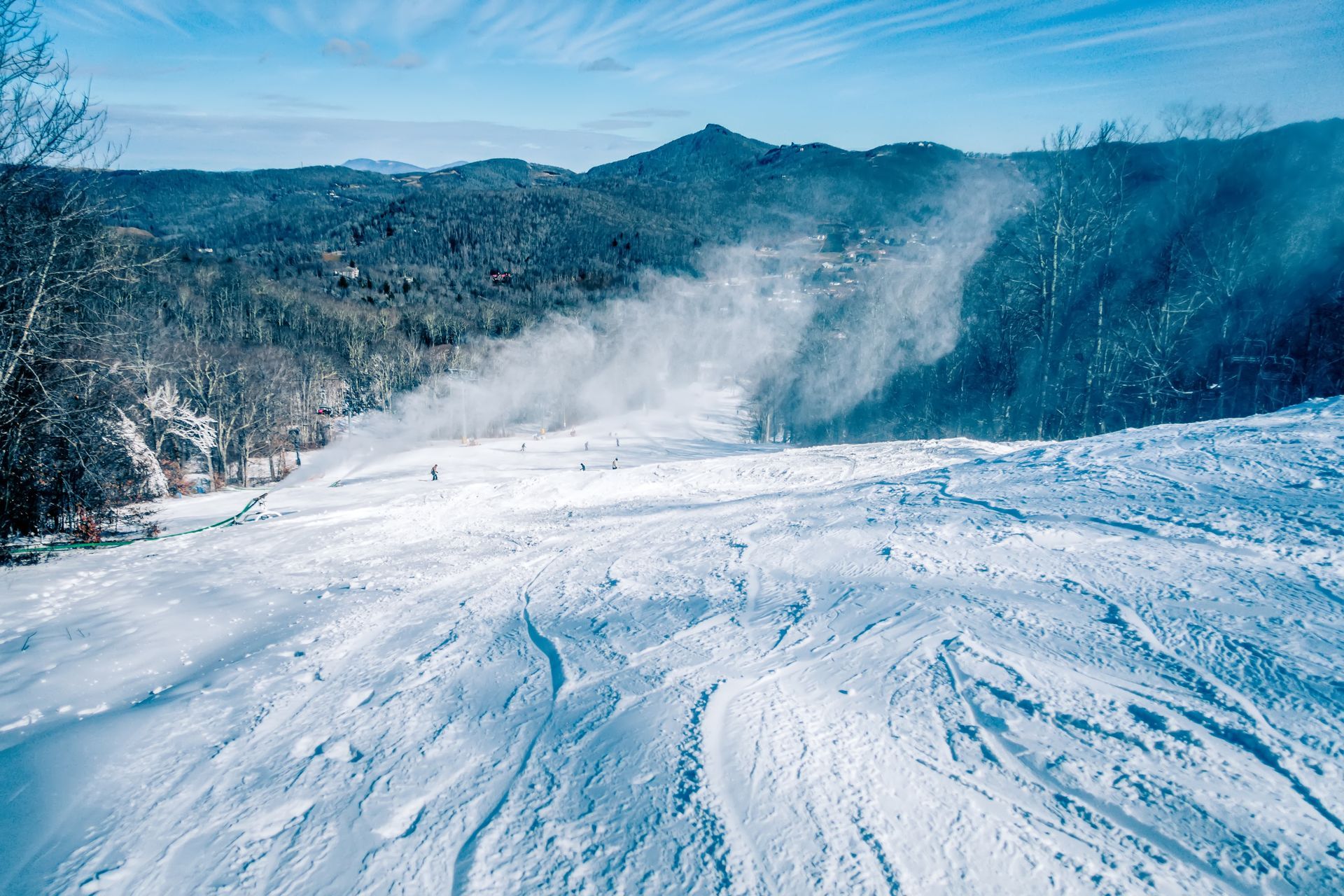 Snow-covered mountain ski slope with tree-lined hills in the background