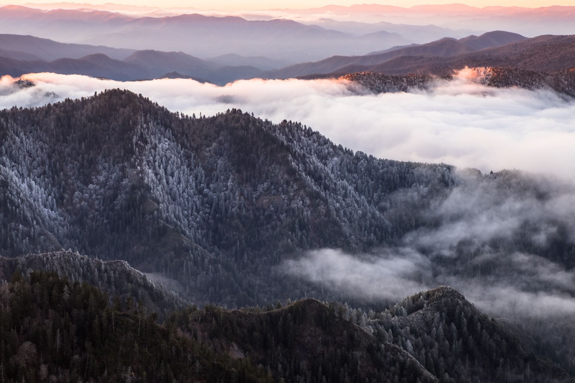 Snowy mountain ridges above a sea of clouds at sunrise
