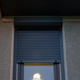 A window with a black shutter on it and a lamp in the window.