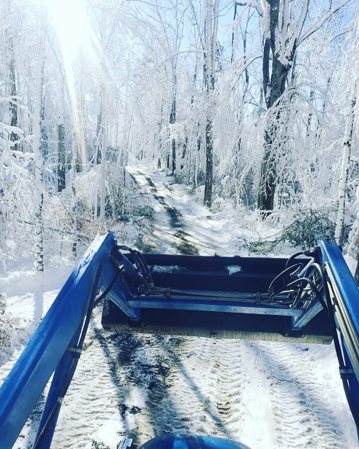 Blue tractor loader on a snowy forest trail with frosted trees in winter