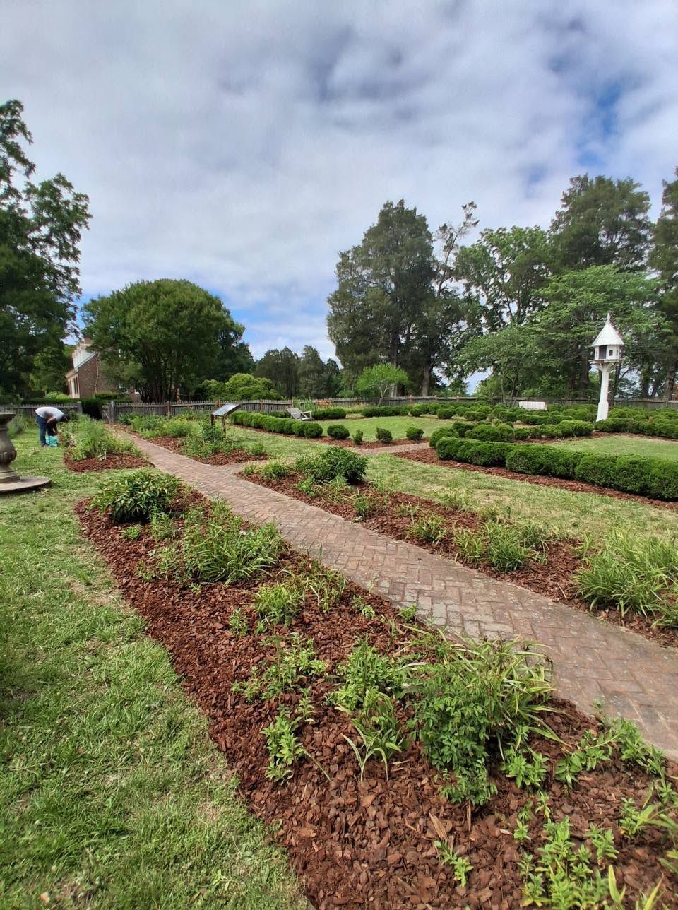 Formal garden with flower beds, gravel paths, and white markers under a cloudy sky