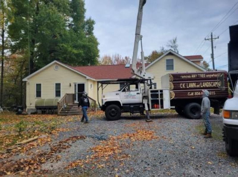 Workers beside a truck and crane in front of a cream house with a red roof on a gravel driveway