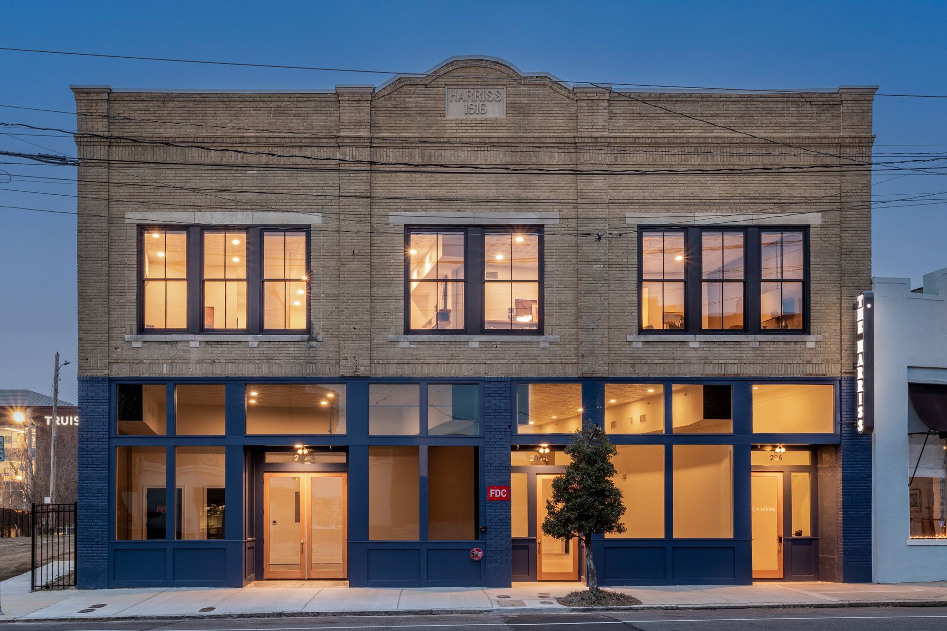 Two-story brick storefront at dusk with lit windows and a blue lower facade