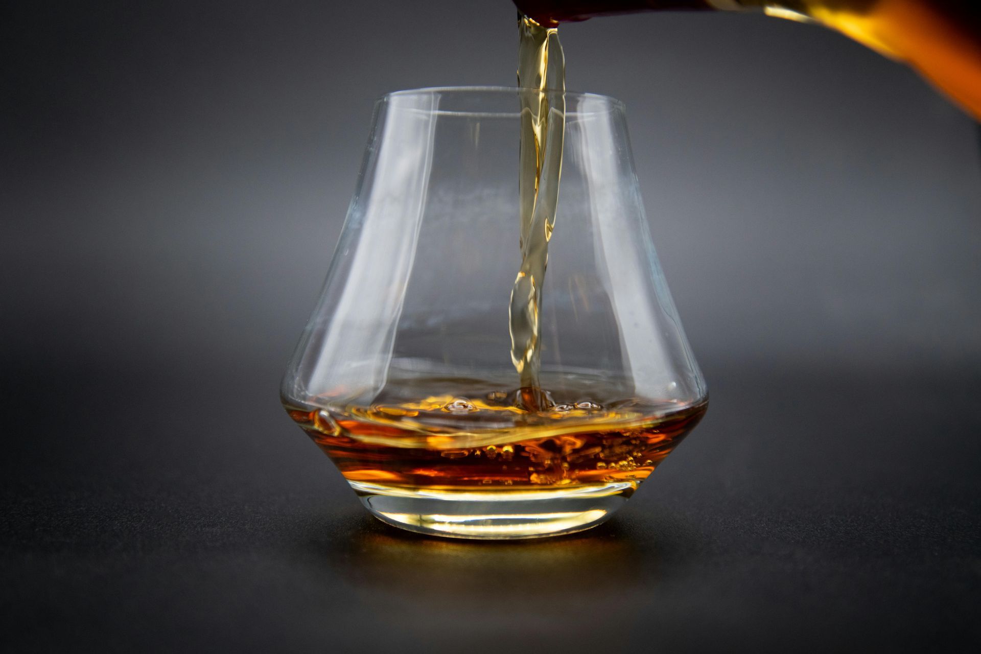 Amber liquor being poured into a clear glass on a dark background