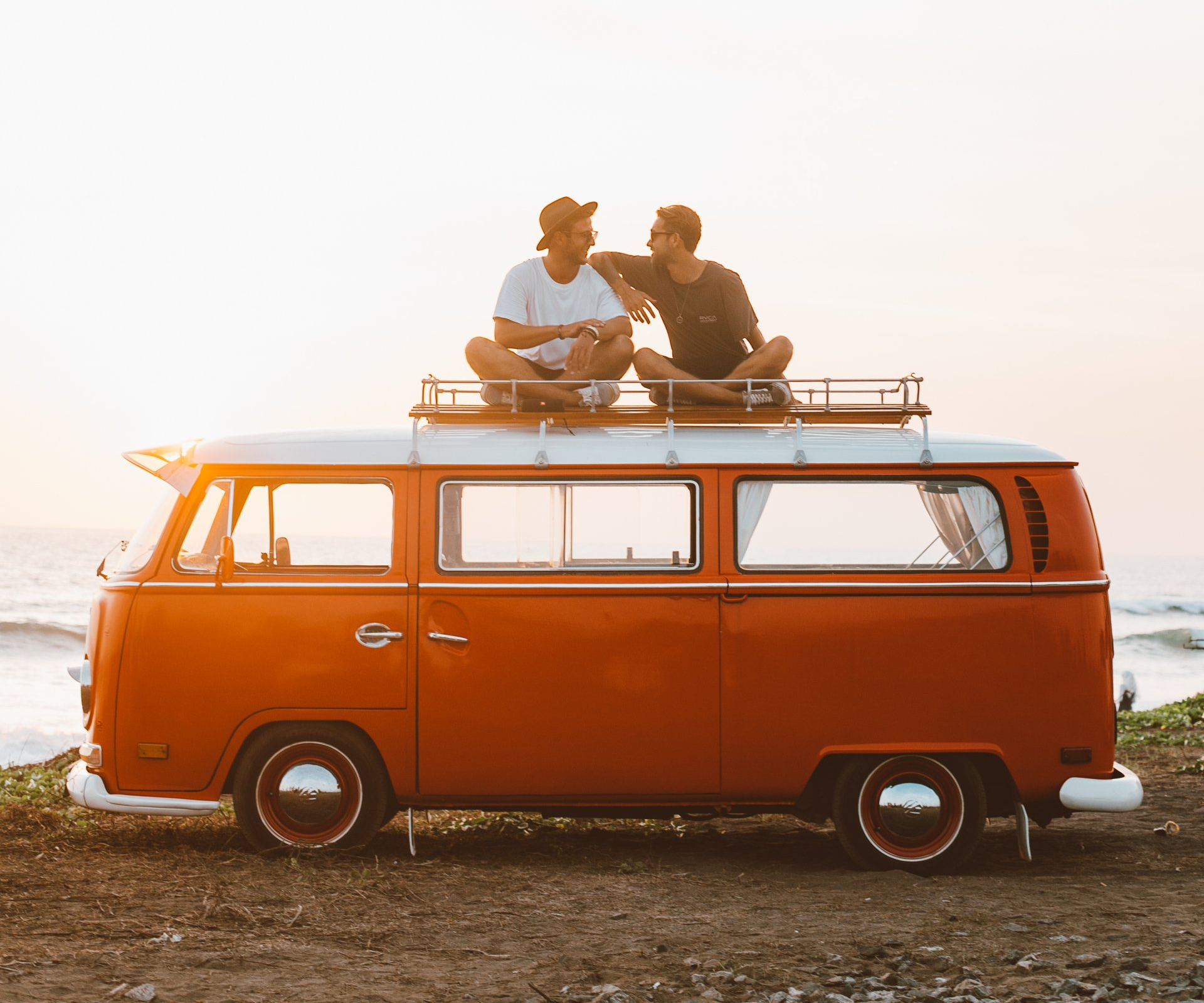 Orange vintage van with two people sitting on the roof at sunset