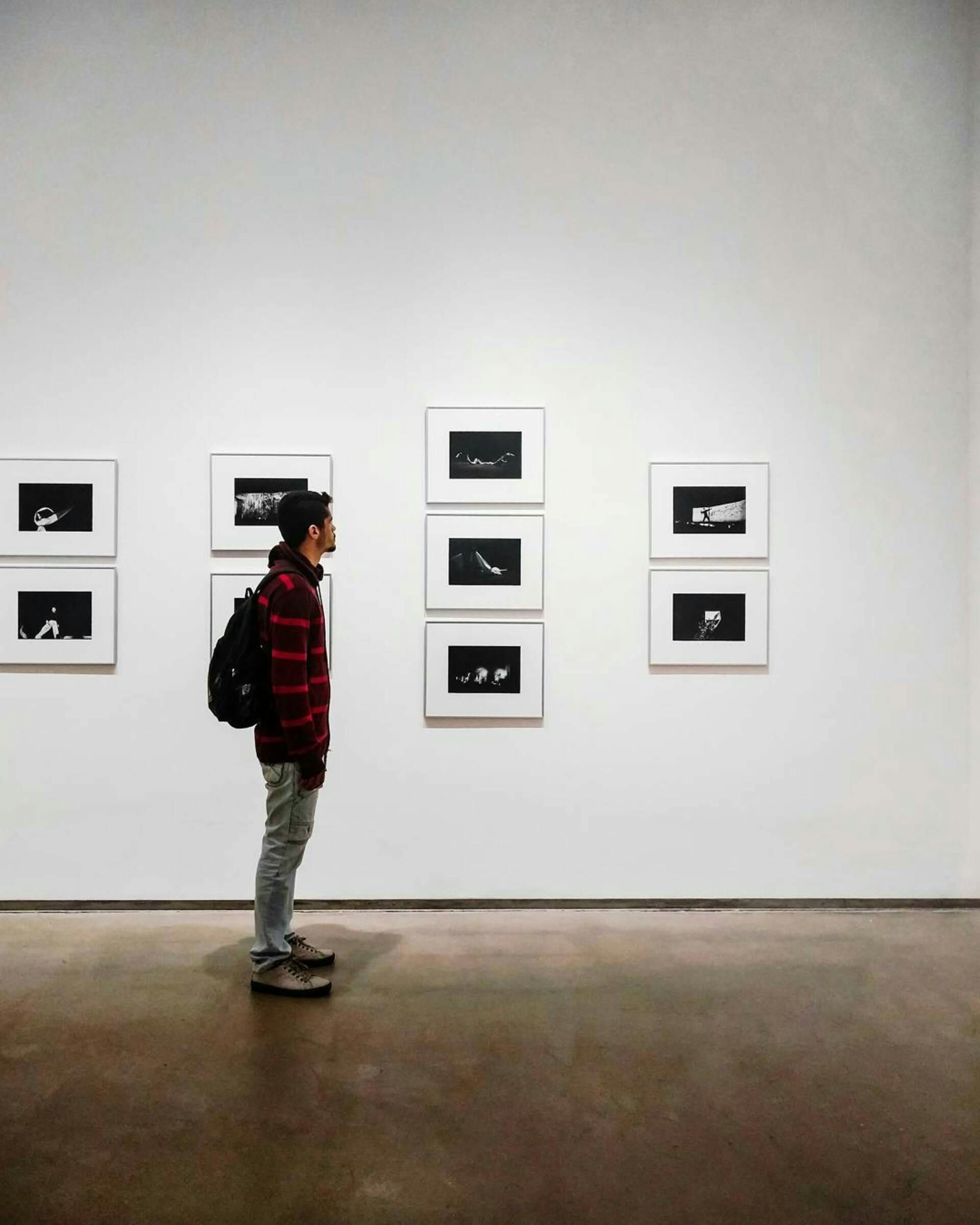 A man with a backpack is standing in front of a wall with pictures on it.