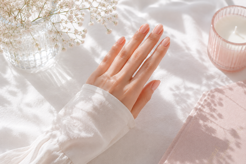 Hand resting on a white blanket beside a pink candle and soft floral shadows