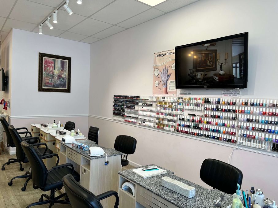 Nail salon interior with manicure tables, chairs, polish displays, wall art, and a TV mounted on the wall