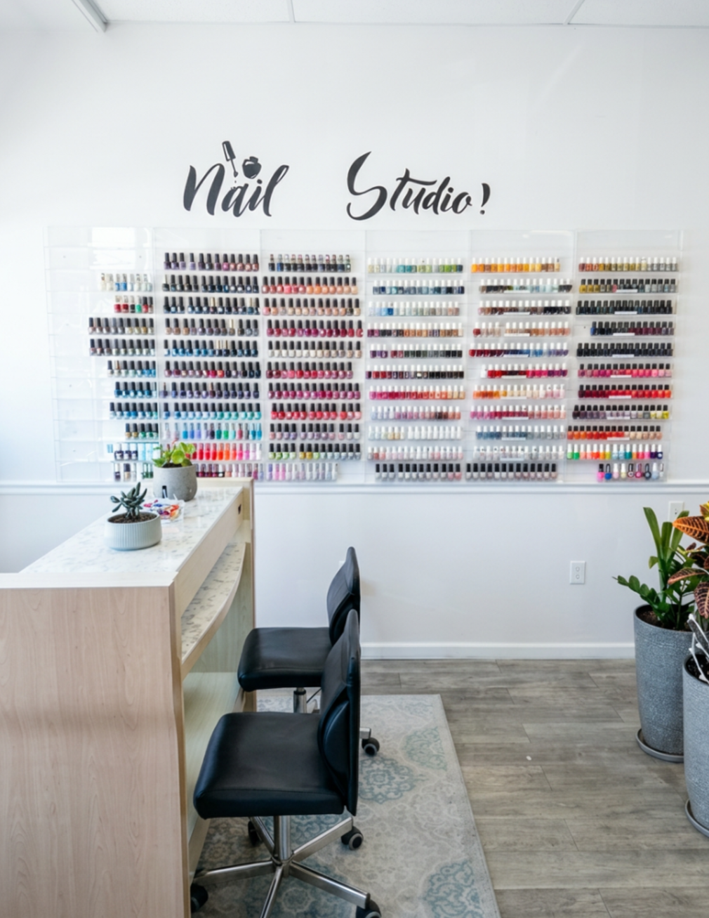 Bright nail studio interior with wall of polish displays, manicure table, and chairs