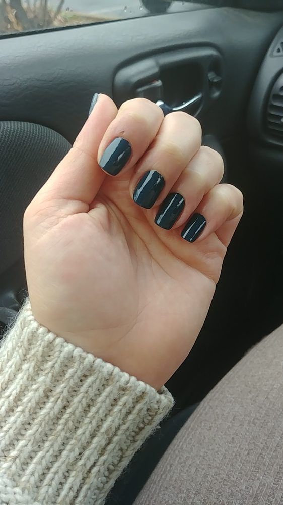 Hand with glossy black nails resting in a car, wearing a beige knit sweater.