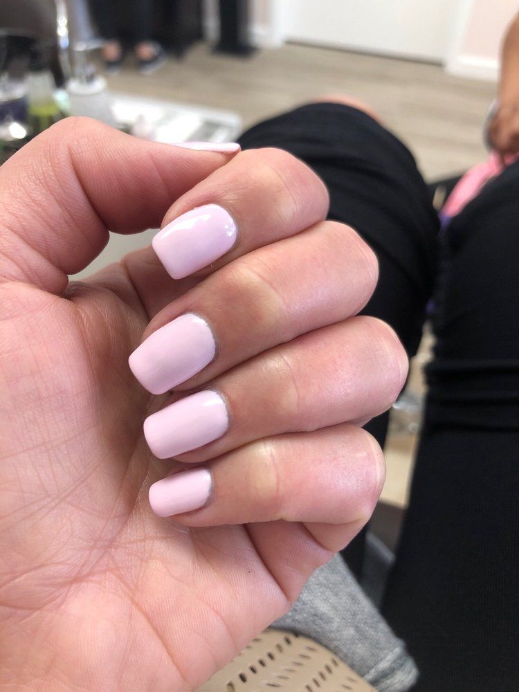 Hand with light pink manicured nails resting on a lap in a casual indoor setting