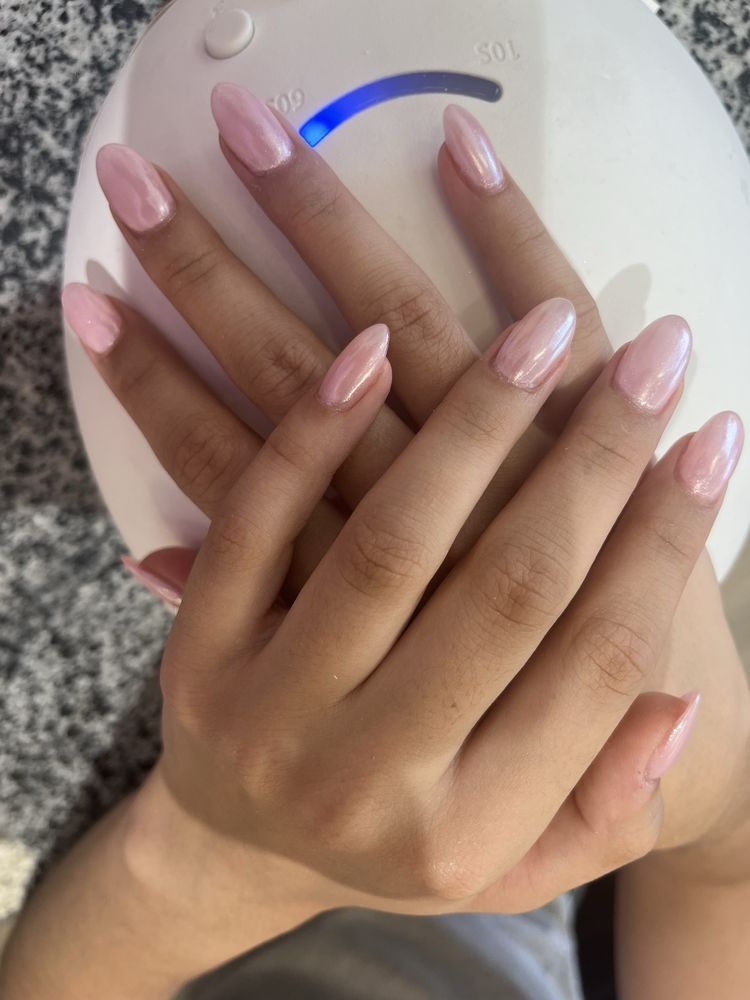 Hands with pale pink manicured nails resting on a white device
