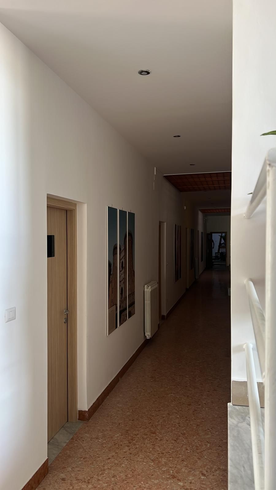Un lungo corridoio con un dipinto sul muro e una porta.