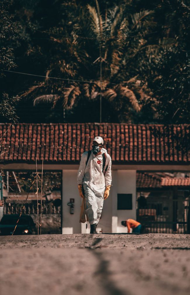 Person in white clothing walking in front of a tiled-roof building with palm trees behind.