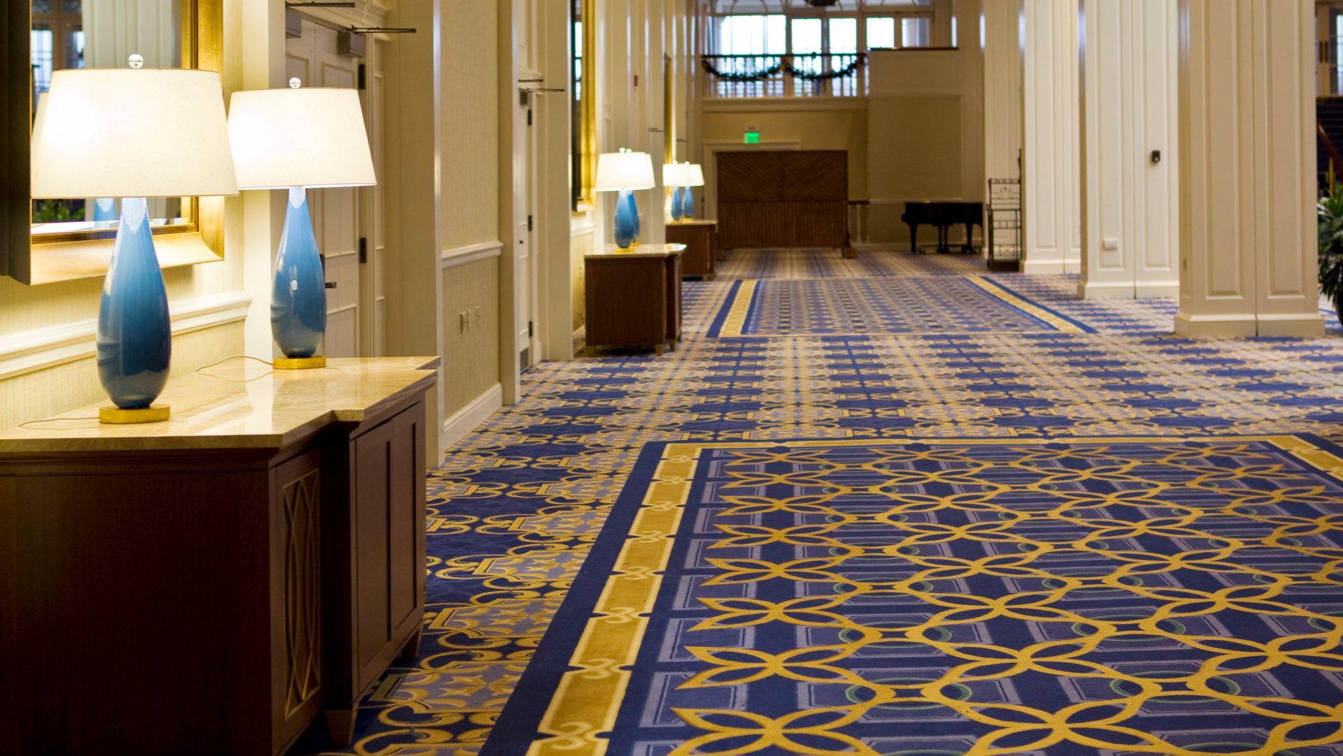 A long hallway with a blue and gold carpet and lamps.