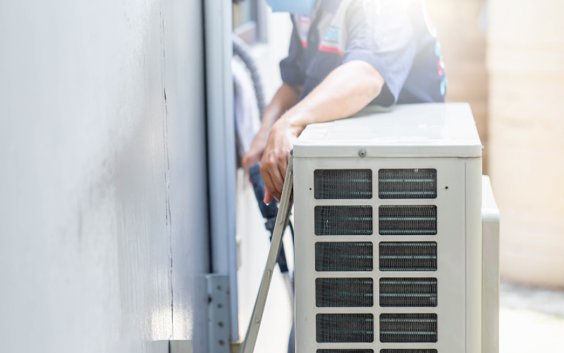 A man is installing an air conditioner on the side of a building.