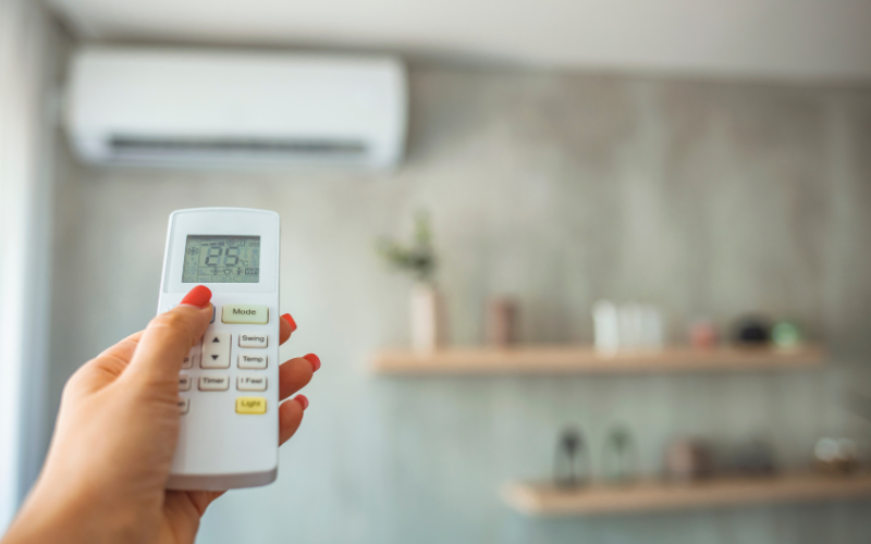 A woman is holding a remote control in front of an air conditioner.