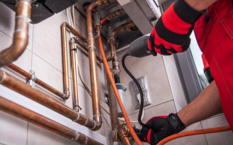 A plumber is working on a copper pipe with a drill.