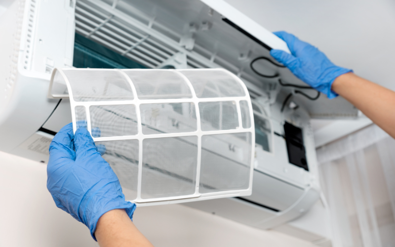 A person wearing blue gloves is cleaning an air conditioner.