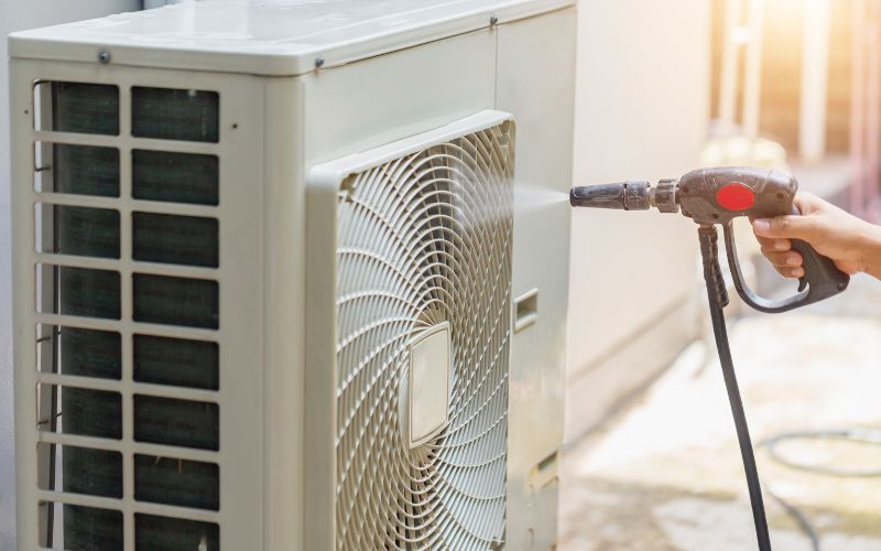 A person is cleaning an air conditioner with a high pressure washer.