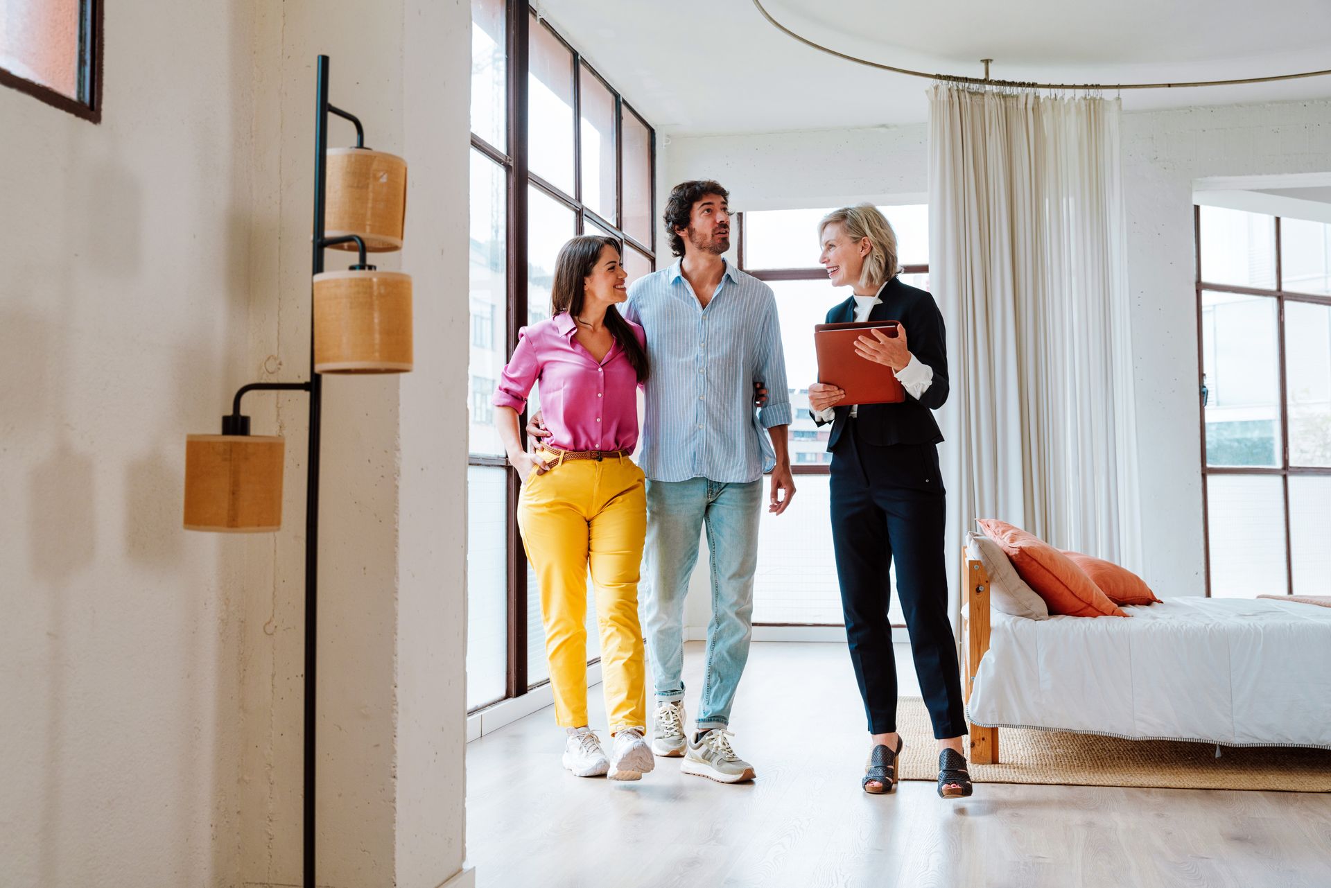 Three people walk through a bright apartment with a real estate agent holding a clipboard.