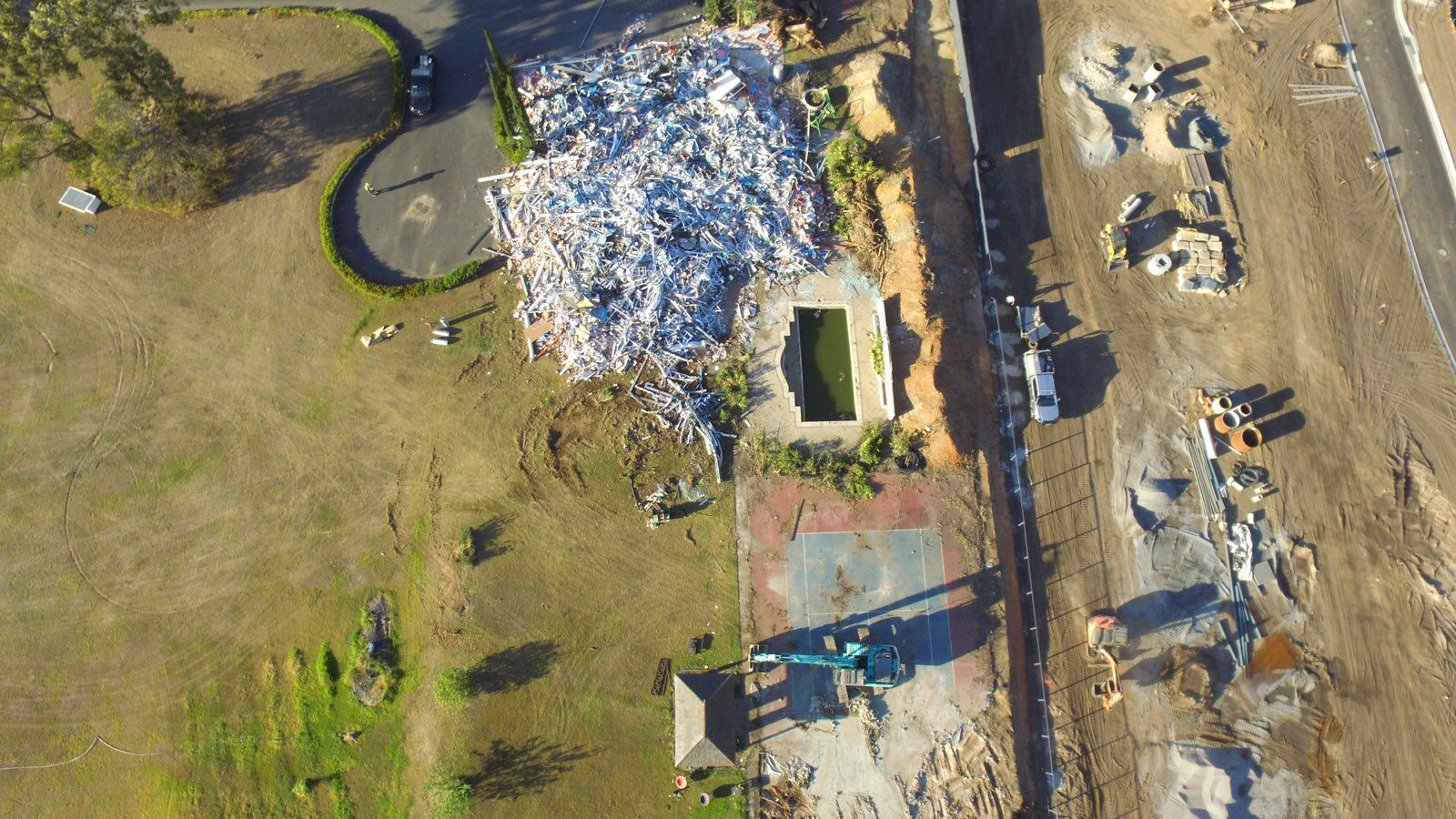 A yellow excavator is demolishing a house behind a fence.