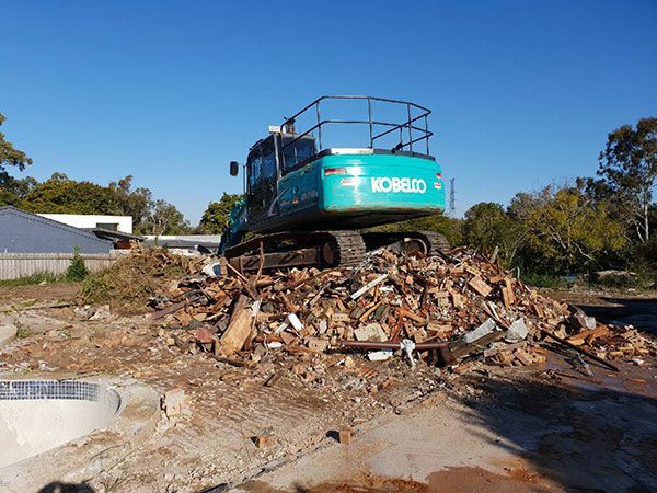 A yellow excavator is demolishing a house behind a fence.