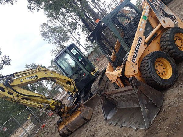 A yellow excavator is demolishing a house behind a fence.