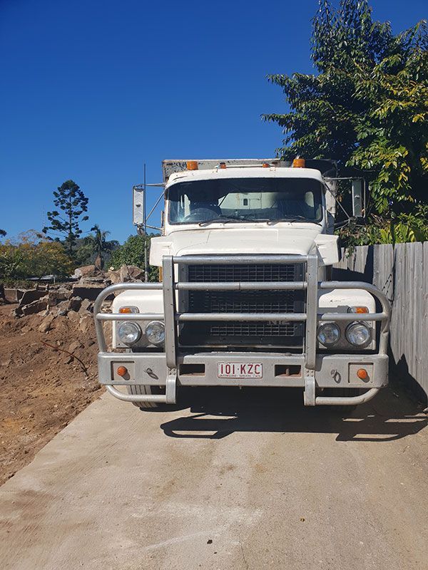 A yellow excavator is demolishing a house behind a fence.