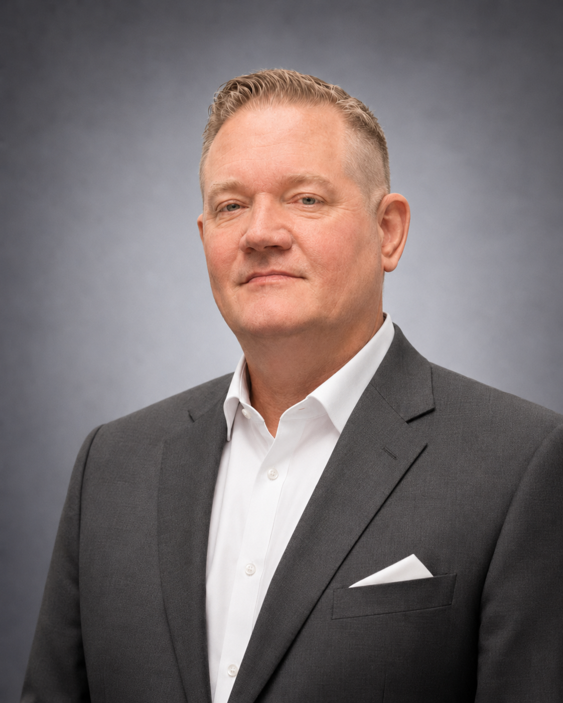 Portrait of a man in a gray suit and white shirt against a gray studio background