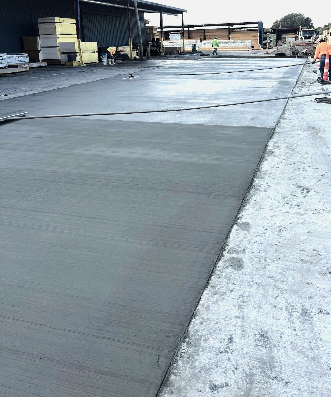 Freshly poured concrete surface, part of a larger construction site, with a worker in the background. Grey tones dominate. Freshly poured concrete surface, part of a larger construction site, with a worker in the background. Grey tones dominate.