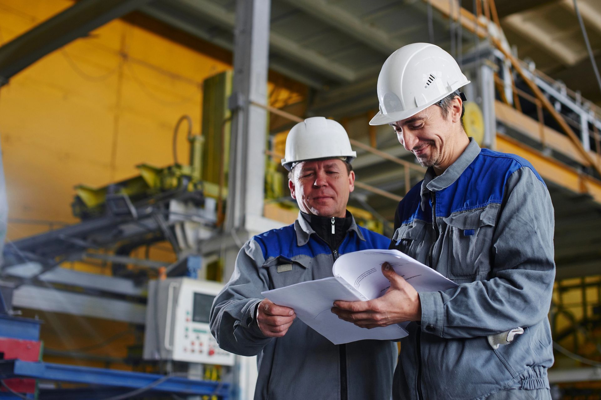 Dos ingenieros con cascos revisando planos en un puesto de trabajo de la fábrica.