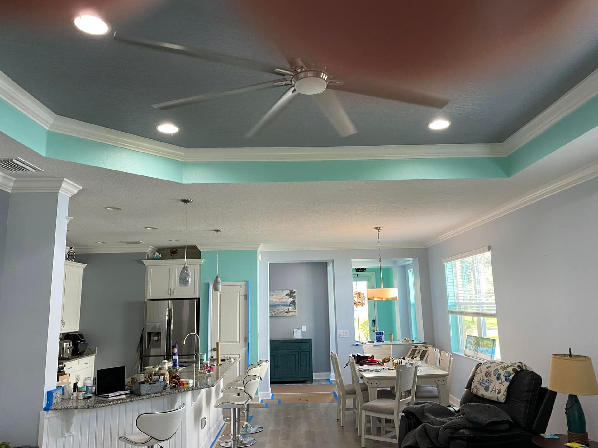 Bright living room with turquoise tray ceiling, white furniture, and a kitchen visible at left.