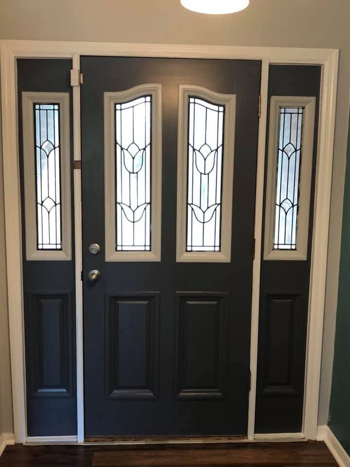 Dark front door with decorative glass sidelights and transom, framed by white trim in an entryway.
