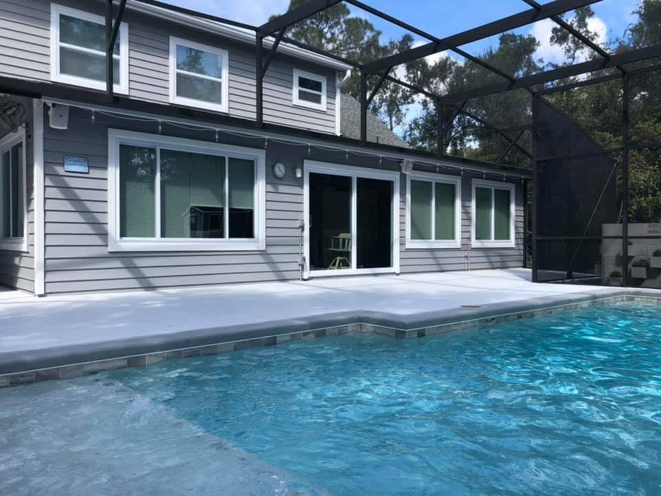 Backyard pool beside a gray house with sliding glass doors and screened enclosure