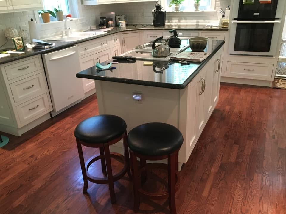 Bright kitchen with a central island, dark stools, black countertops, and hardwood floors.
