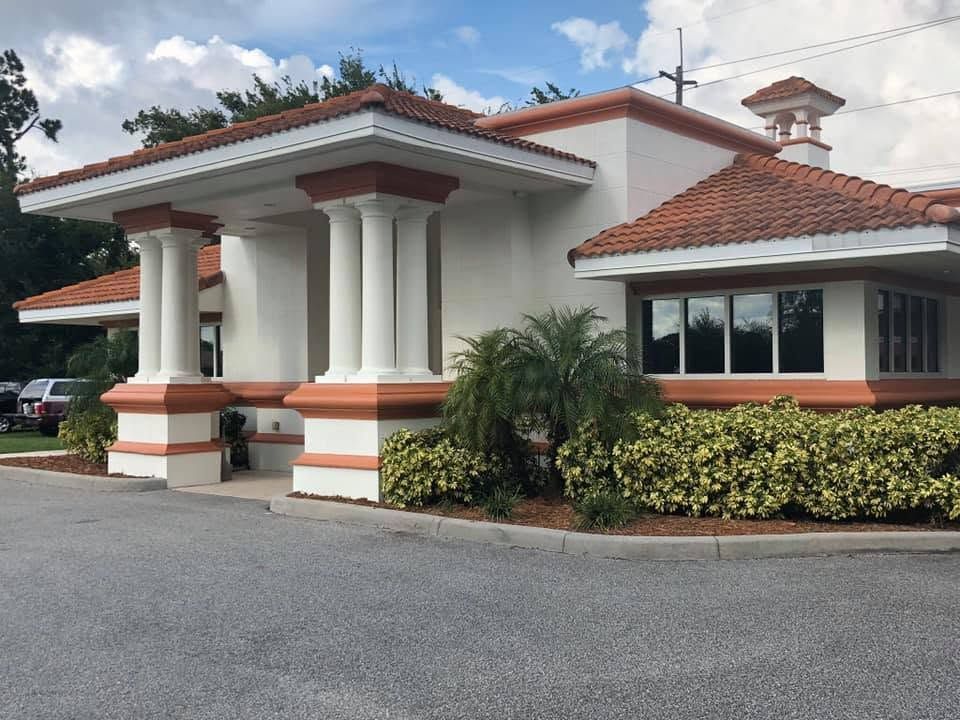 Entrance to a white stucco building with red tile roof and orange trim, beside hedges and a driveway