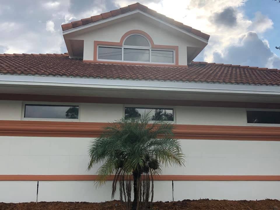 White stucco house with red-tile roof and arched window, seen behind a palm tree