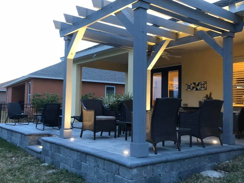 Back patio with pergola, outdoor seating, and warm lights beside a brick house.