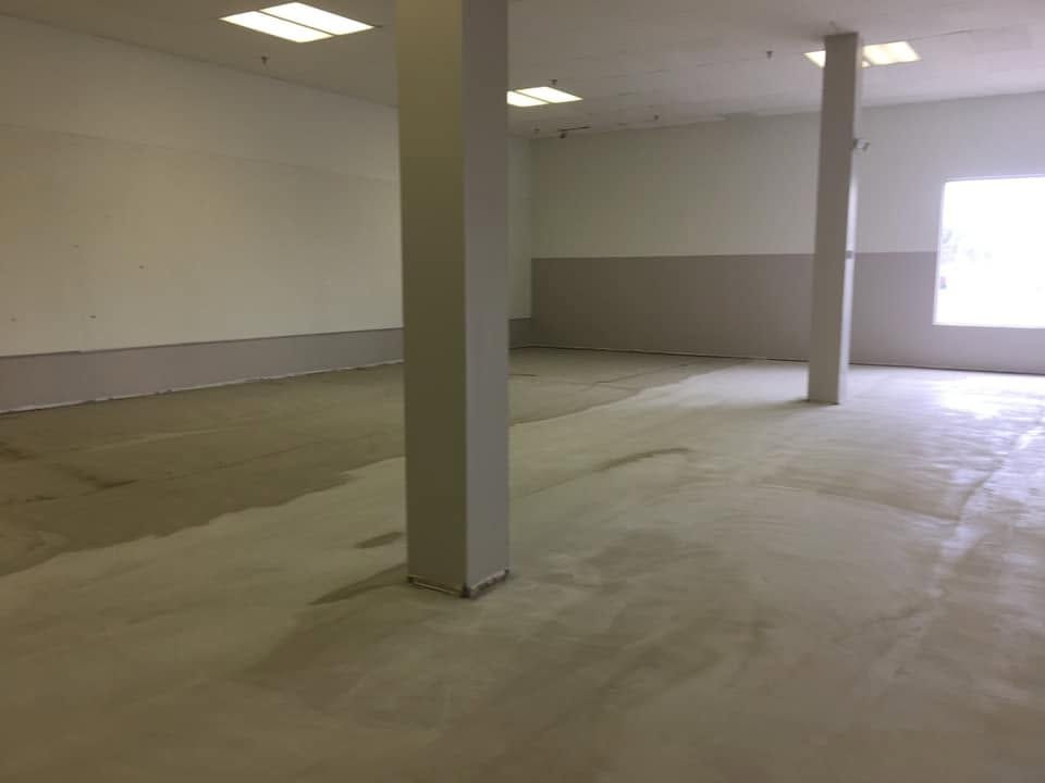 Empty unfinished room with white columns, bare concrete floor, and a bright window.